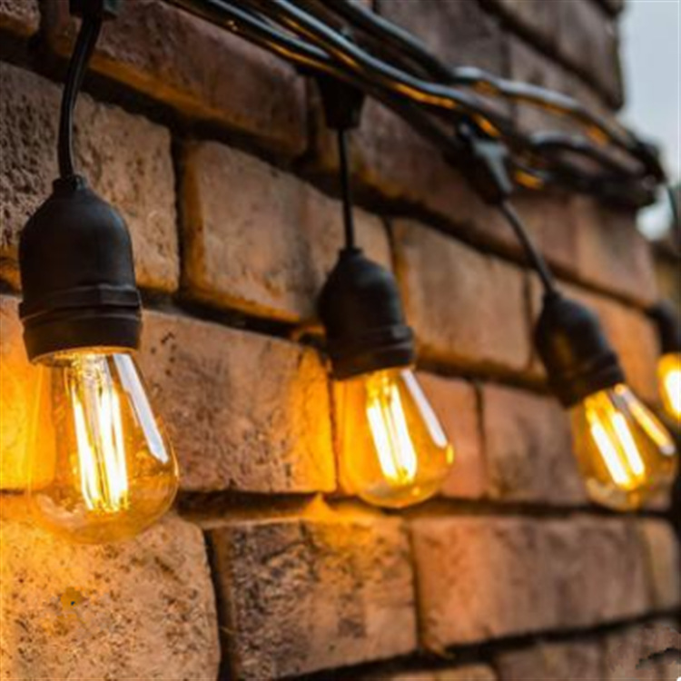 Warm string-light bulbs hanging from black cable against a brick wall